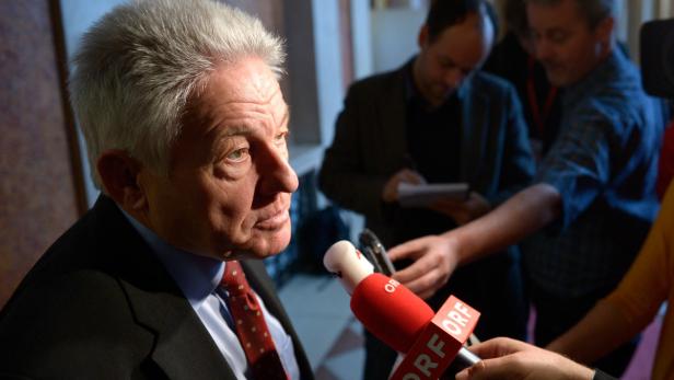 Ein Mann mit grauem Haar wird von Reportern interviewt.