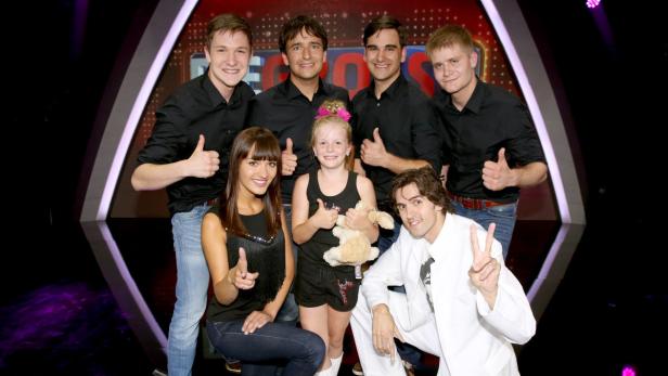 Eine Gruppe von Menschen posiert vor einem Studiohintergrund und zeigt Daumen hoch.