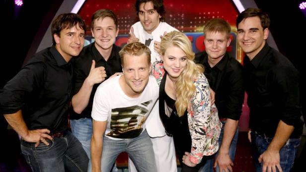 Eine Gruppe von sieben Personen posiert lächelnd vor einem roten Hintergrund.