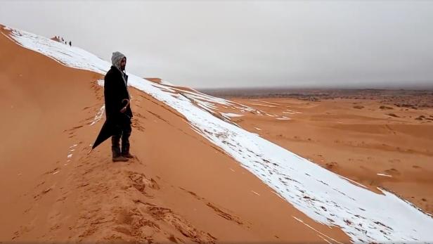 Ein Mann steht in der Sahara und schaut sich den Schnee an