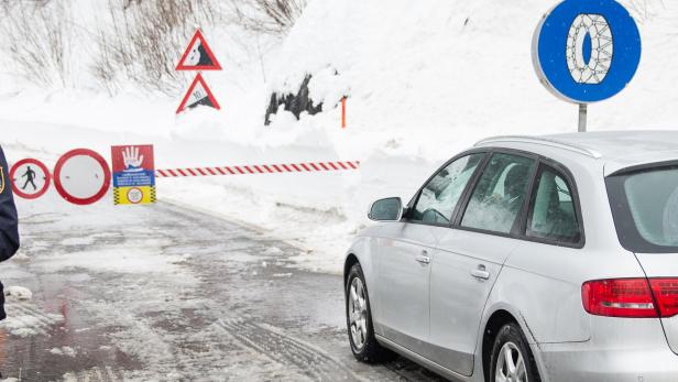 Ein silberner Kombi steht vor einer gesperrten, schneebedeckten Straße mit Warnschildern.