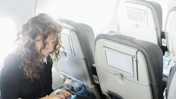 Eine Frau sitzt im Flugzeug und benutzt ihr Smartphone.