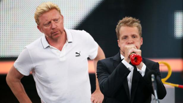 Boris Becker und ein Mann im Anzug, der in eine rote Paprika bläst.