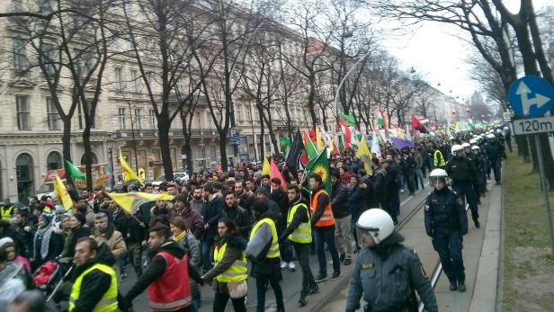 Eine Demonstration mit vielen Menschen und kurdischen Flaggen zieht durch eine Stadt.