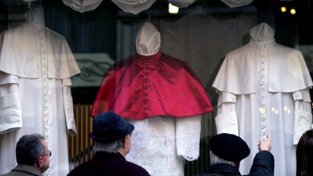 People look at three Papal vestments displayed in the Gammarelli&#039;s tailor shop window in Rome April 14, 2005. Cardinals start choosing a new Pope next week but the successor to John Paul will be all sewn up well before the secret conclave opens. Because the tailor Filippo Gammarelli has no clue as to who the new pope will be, the firm has made three versions of the same silk and wool outfit, in small, medium and large, to clothe the most lean or corpulent cardinal. REUTERS/Alessia Pierdomenico