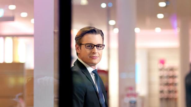 Ein Mann mit Brille und Anzug steht vor einem Schaufenster.