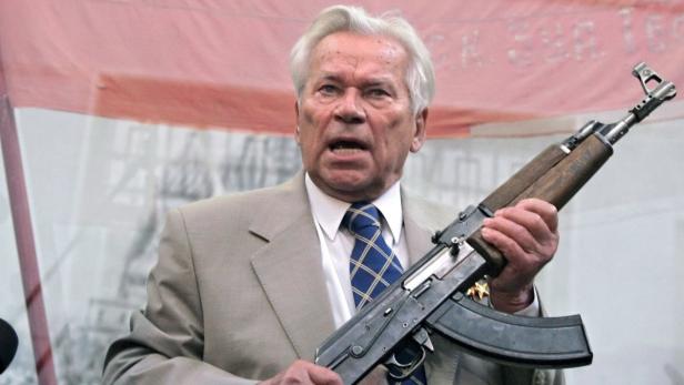 Ein älterer Mann im Anzug hält ein AK-47-Gewehr in der Hand.