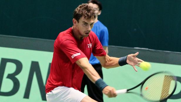 Ein Tennisspieler in rotem Hemd schlägt einen gelben Tennisball.