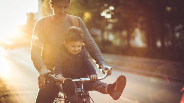 Ein Vater fährt mit seinem kleinen Sohn auf dem Fahrrad im goldenen Abendlicht.