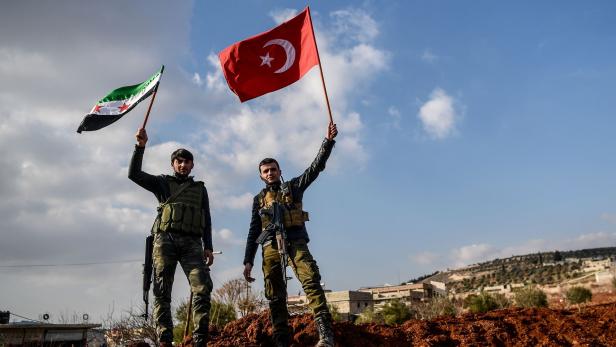 TOPSHOT - A Turkish-backed Syrian rebel fighters hold Turkish national flag (R) and Free Syrian Army flags (L) at a checkpoint in the Syrian town of Azaz on a road leading to Afrin, on February 1, 2018. Clashes raged between Turkish-backed forces and Kurdish militia in Syria&#039;s Afrin region on January 31, 2018, as wounded civilians fled intense Turkish air strikes. Turkey and allied Syrian rebels have pressed on with Operation Olive Branch in the Kurdish-controlled Afrin enclave despite mounting international concern and reports of rising civilian casualties. / AFP PHOTO / OZAN KOSE