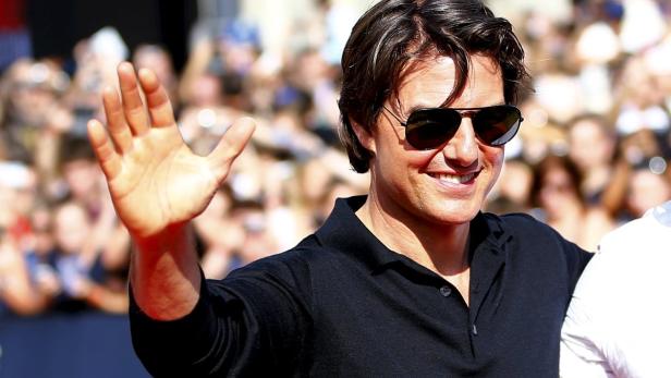 Tom Cruise lächelt und winkt mit Sonnenbrille vor einer Menschenmenge.