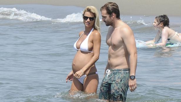 Eine schwangere Frau im Bikini steht mit einem Mann im Meer.