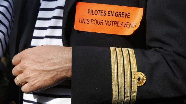 Ein Pilot mit einer orangefarbenen Notiz „Pilotes en greve unis pour notre avenir“ an seiner Uniform.