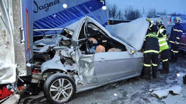 Ein schwerer Autounfall im Schnee, bei dem ein Auto unter einen Lastwagen geraten ist. Rettungskräfte sind vor Ort.