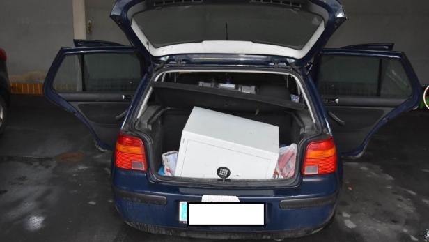Ein blauer VW Golf mit geöffneter Heckklappe und einem weißen Safe im Kofferraum.