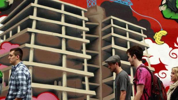 Eine Gruppe von Menschen geht an einem Graffiti mit Wolkenkratzern und einem Drachen vorbei.