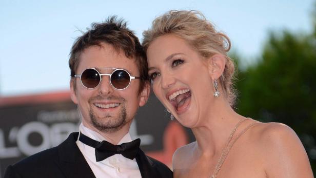 Kate Hudson und Matt Bellamy lächeln auf einem roten Teppich.