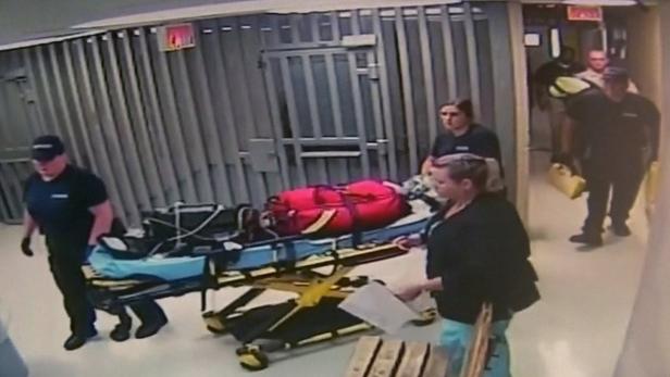Sanitäter schieben eine Person auf einer Trage durch einen Flur.