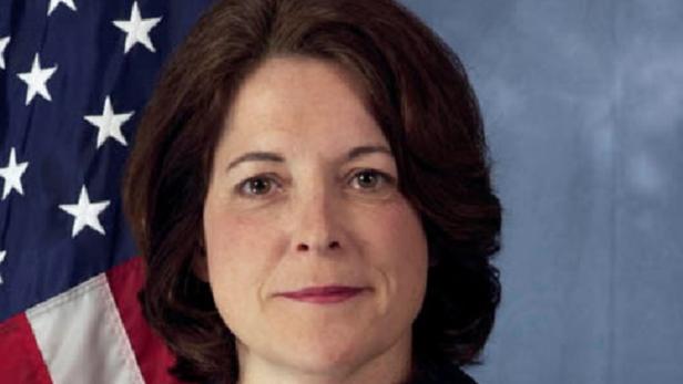 Eine Frau mit braunen Haaren vor einer amerikanischen Flagge.