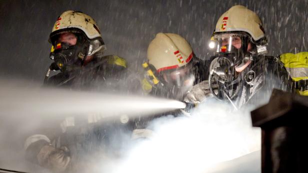 Drei Feuerwehrleute mit Atemschutzgeräten spritzen Wasser.