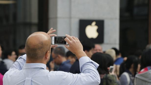 Ein Mann fotografiert mit seinem Smartphone das Apple-Logo an einem Gebäude.