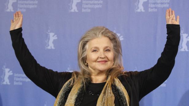 Die Schauspielerin Hanna Schygulla posiert mit erhobenen Armen vor einem Hintergrund der Berlinale.