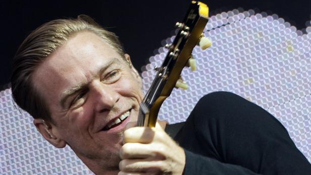 Bryan Adams spielt Gitarre und lächelt.