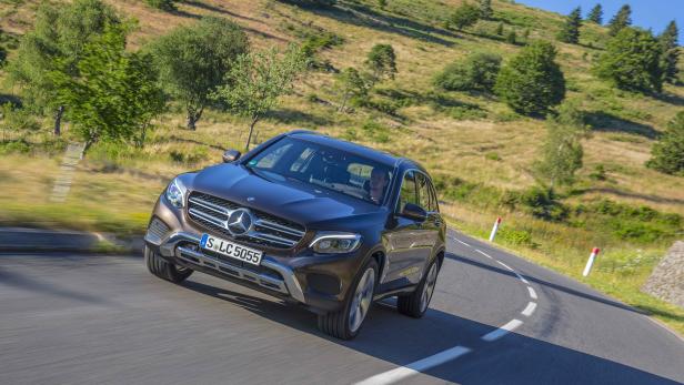 Ein brauner Mercedes-Benz fährt auf einer kurvenreichen Bergstraße.
