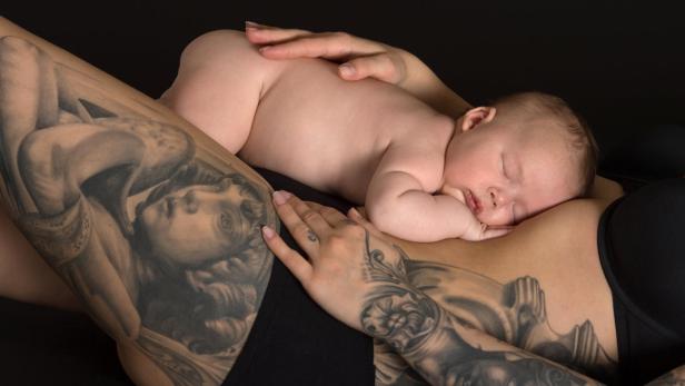 Ein schlafendes Baby liegt auf dem Bauch einer tätowierten Frau.