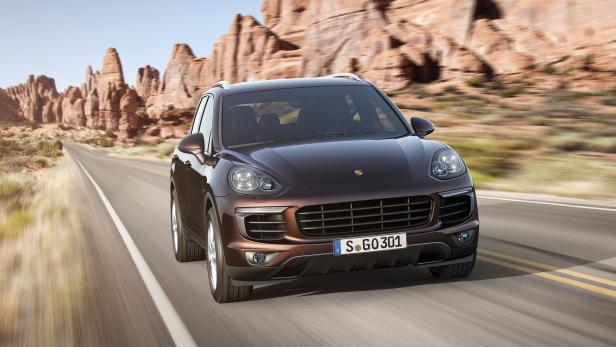 Ein brauner Porsche Cayenne fährt auf einer Straße durch eine Wüstenlandschaft.