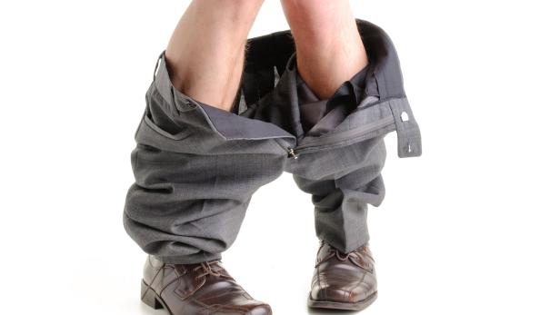 Symbolbild Urinieren: Waden und Füße eines Mannes mit heruntergelassener Hose