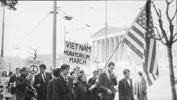 Jugendliche mit Transparent &quot;Vietnam Moratorium March&quot; und USA-Fahne marschieren über den Ring, im Hintergrund das Parlament