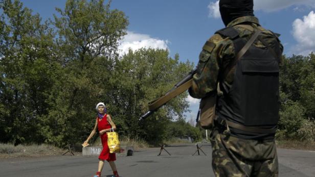 Eine ältere Frau in Rot überquert eine Straße, bewacht von einem bewaffneten Soldaten.