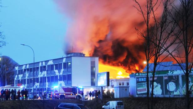 Ein Gebäude steht in Flammen, während Feuerwehrleute und Schaulustige zusehen.