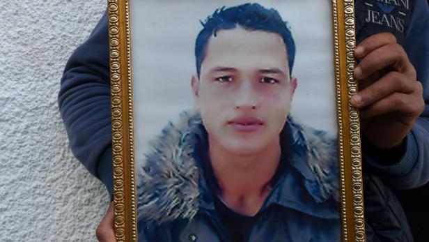 (FILES) This file photo taken on December 23, 2016 shows Walid Amri (back), the brother of 24-year-old Anis Amri, the Berlin Christmas market attacker, posing with a portrait of his brother in front of the family house in the town of Oueslatia, in Tunisia&#039;s region of Kairouan. A special investigator commissioned by the Berlin Senate will present his final report on October 12, 2017 on the case and on possible mistakes of the police. Amri had killed 12 people with a truck at a Berlin Christmas market on December 19, 2016. / AFP PHOTO / FETHI BELAID
