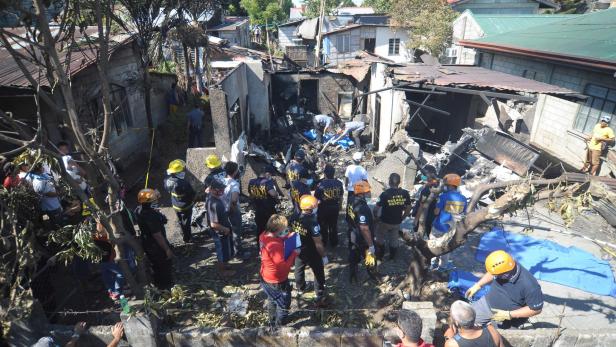 Rescuers and investigators stand at the site where a twin-engined plane crashed into a house just after taking off in Plaridel town, Bulacan province, north of Manila on March 17, 2018. At least seven people were killed when a small plane crashed into house while trying to take off just outside the Philippine capital on Saturday, police and aviation officials said. / AFP PHOTO / STR