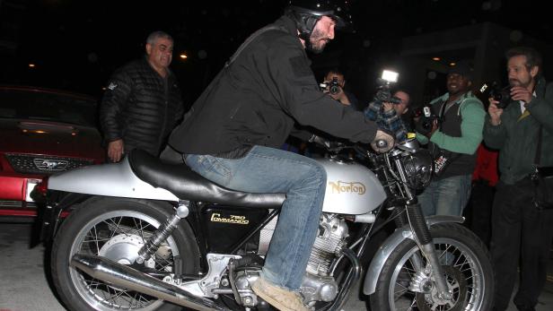 Keanu Reeves auf einem Norton Commando Motorrad, umringt von Fotografen.