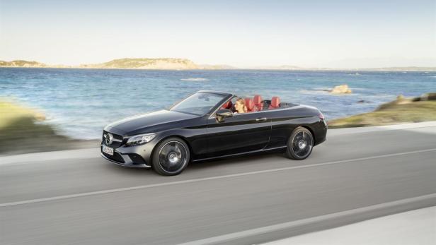 Ein schwarzes Mercedes-Benz C-Klasse Cabriolet fährt an einer Küstenstraße entlang.