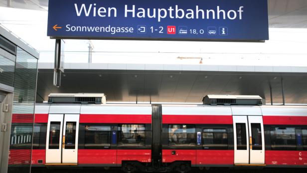 Ein roter Zug steht am Wiener Hauptbahnhof unter einem Wegweiser.