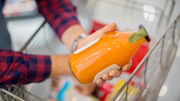 Man hälft Flasche mit Karottensaft über seinem Einkaufswagen im Supermarkt.