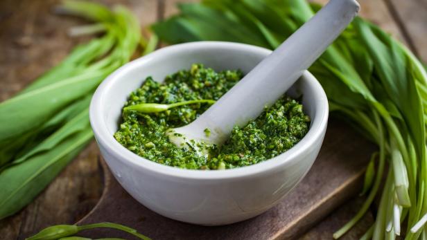 Ein Mörser mit Bärlauchpesto steht auf einem Holztisch.