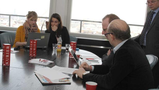 Mehrere Personen sitzen an einem Tisch und arbeiten an Laptops und Dokumenten.