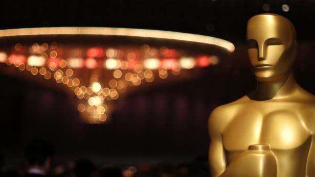 Eine goldene Oscar-Statue vor einem unscharfen Hintergrund mit einem Kronleuchter.