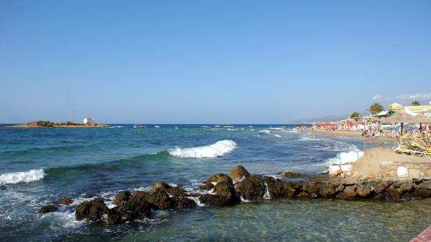 Ein belebter Strand mit Sonnenschirmen und Badegästen an einem sonnigen Tag.