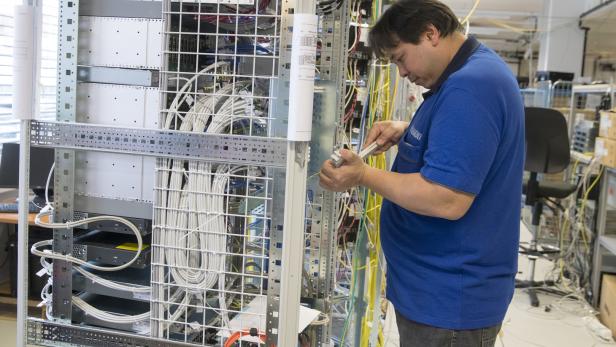 Ein Techniker arbeitet an einem Serverschrank mit vielen Kabeln.