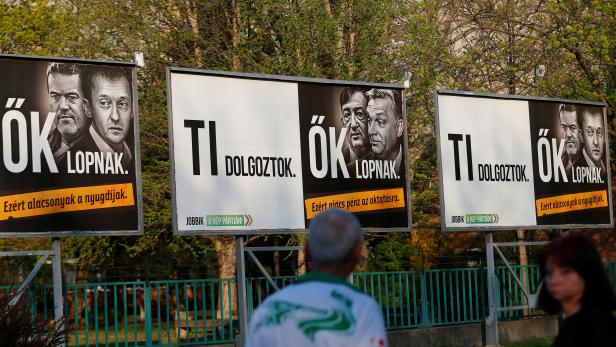 Pedestrians pass by posters showing Hungarian Prime Minister Viktor Orban and his associates in Budapest