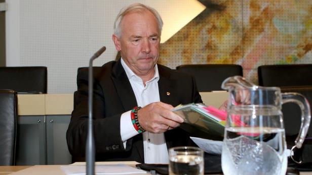 Ein Mann in einem Anzug sitzt an einem Tisch mit Papieren und einem Wasserkanne.