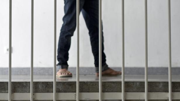 Eine Person in Jeans und Sandalen steht hinter Gittern.