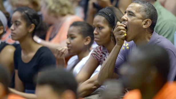 Barack Obama isst Popcorn mit seiner Familie bei einem Basketballspiel.
