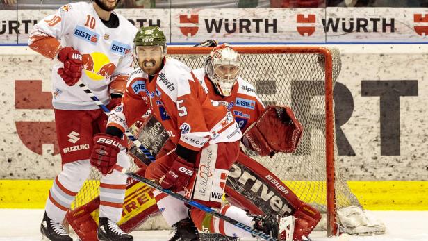Drei Eishockeyspieler in roter und weißer Spielkleidung stehen auf dem Eis vor einem Tor.